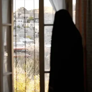 نمای از زن محجبه رو به منظره روستایی از پنجره